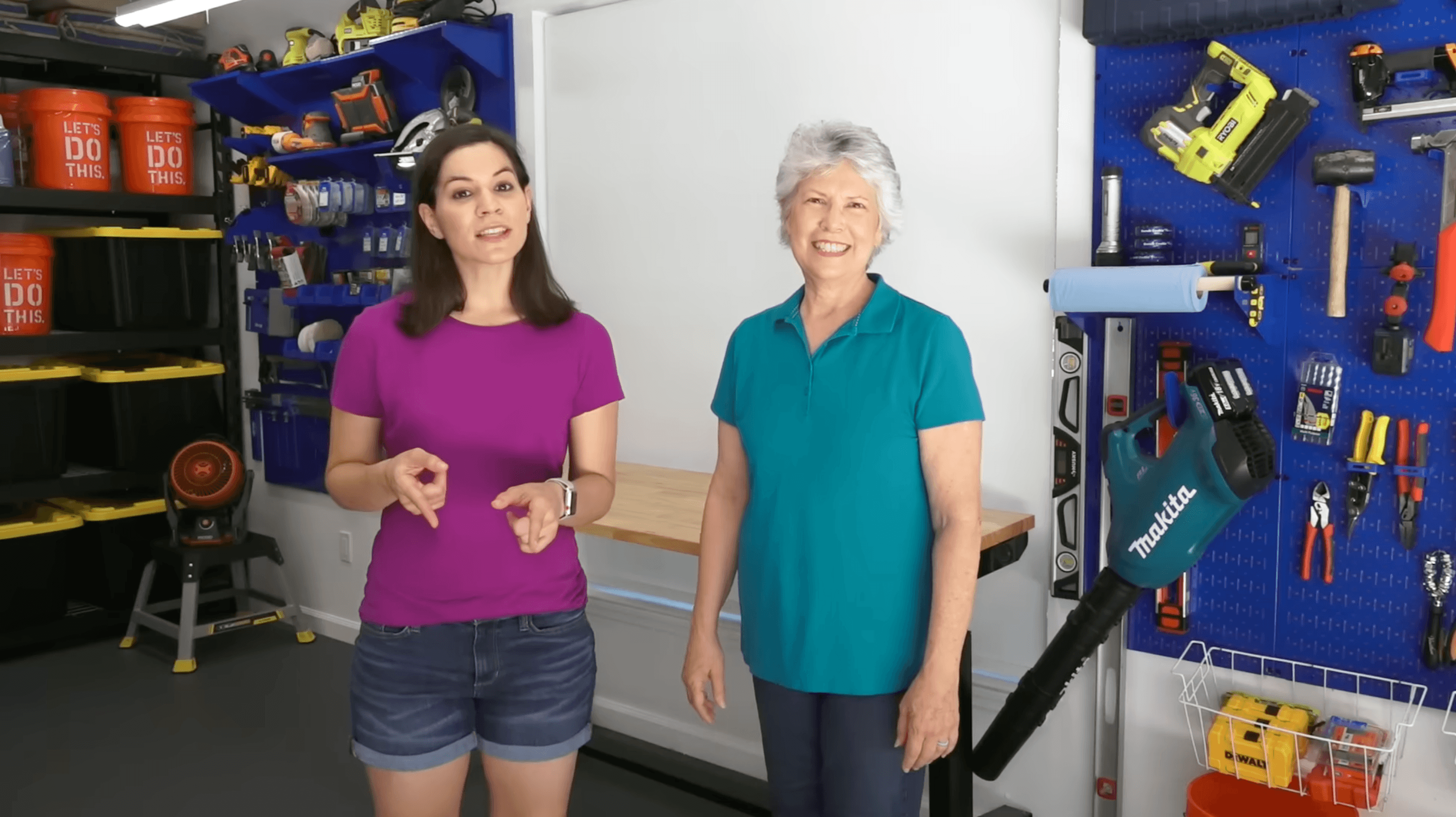 Two women standing in a garage with tools and equipment on shelves.