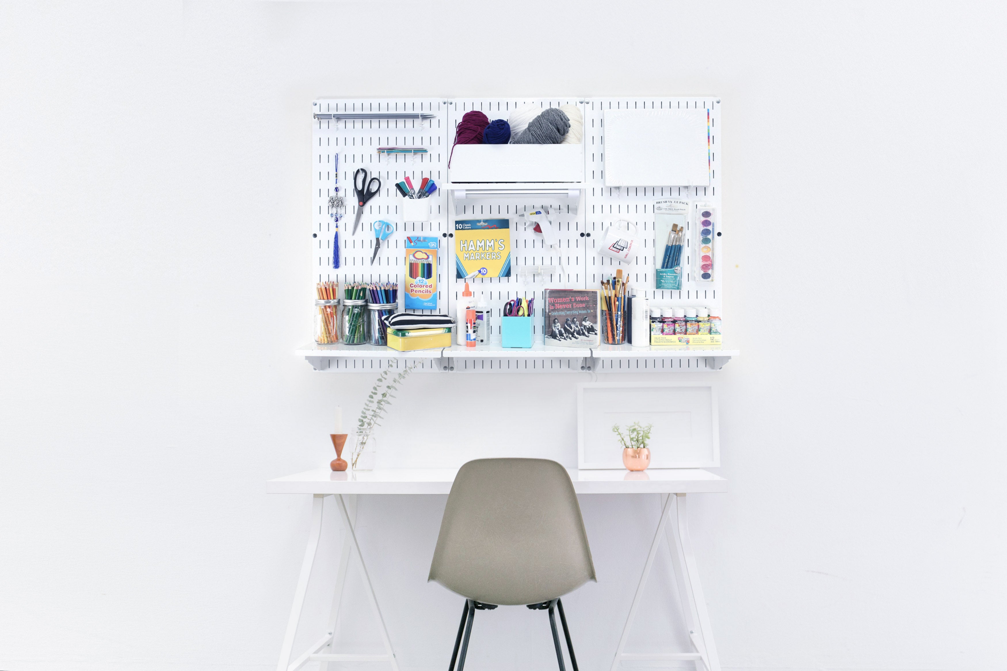 White desk with various stationery items on a pegboard and a chair against a white wall