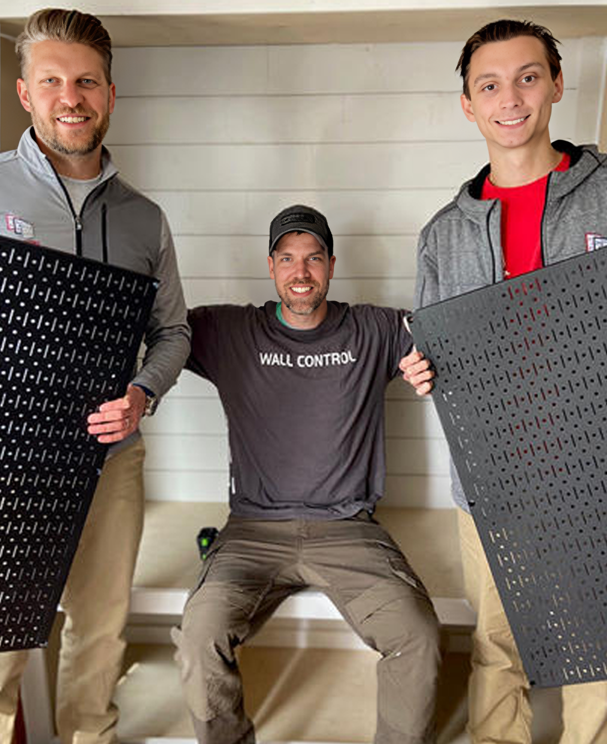 Three men holding large black mats with 'Wall Control' branding in a room.