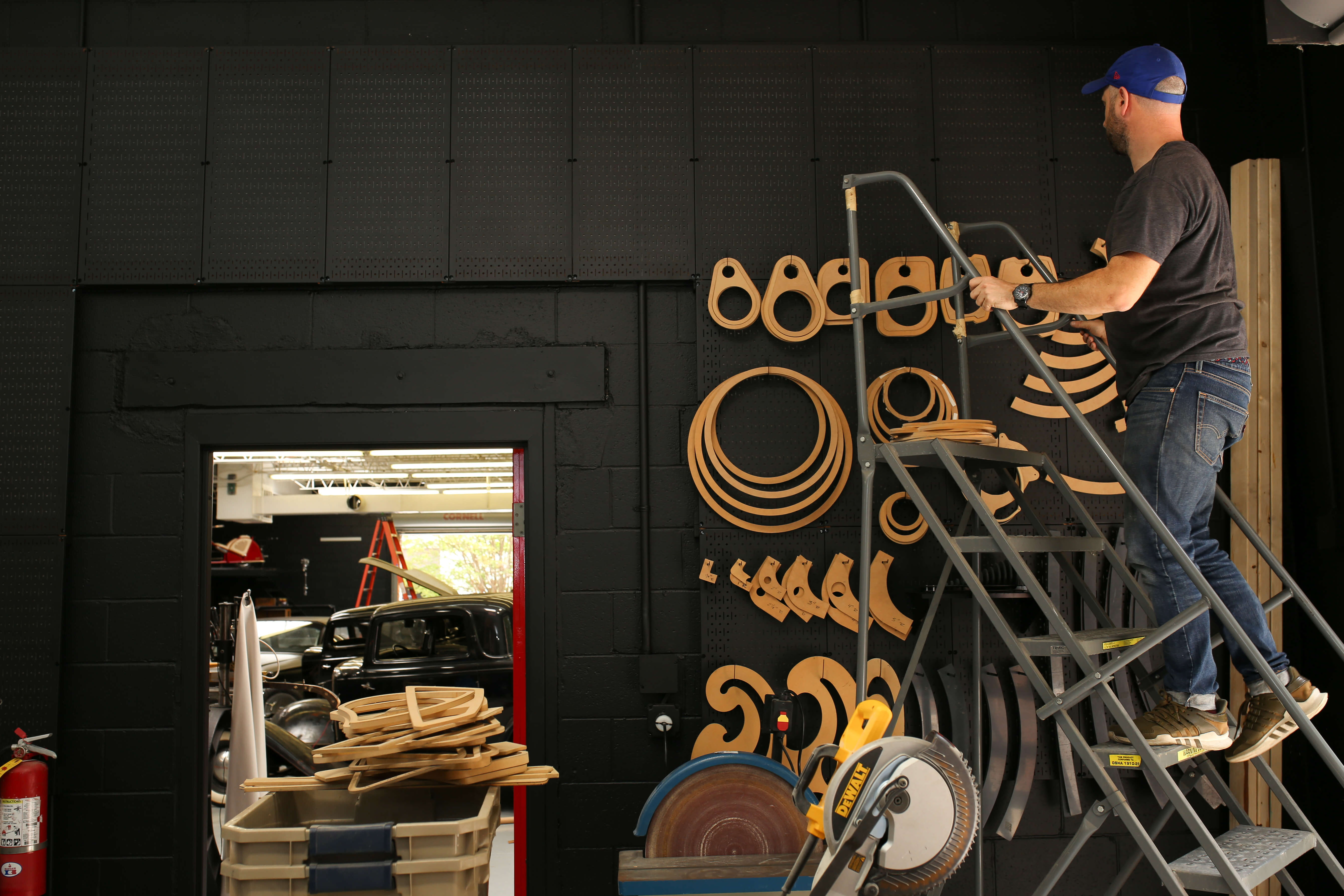 Man working on a decorative pegboard wall with circular patterns in a workshop.